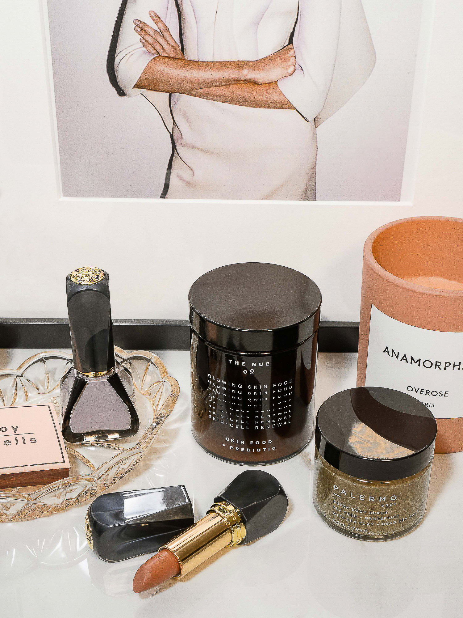 Close-up of beauty and skincare products including lipstick, nail polish, face cream, and candle in a bright, indoor setting.