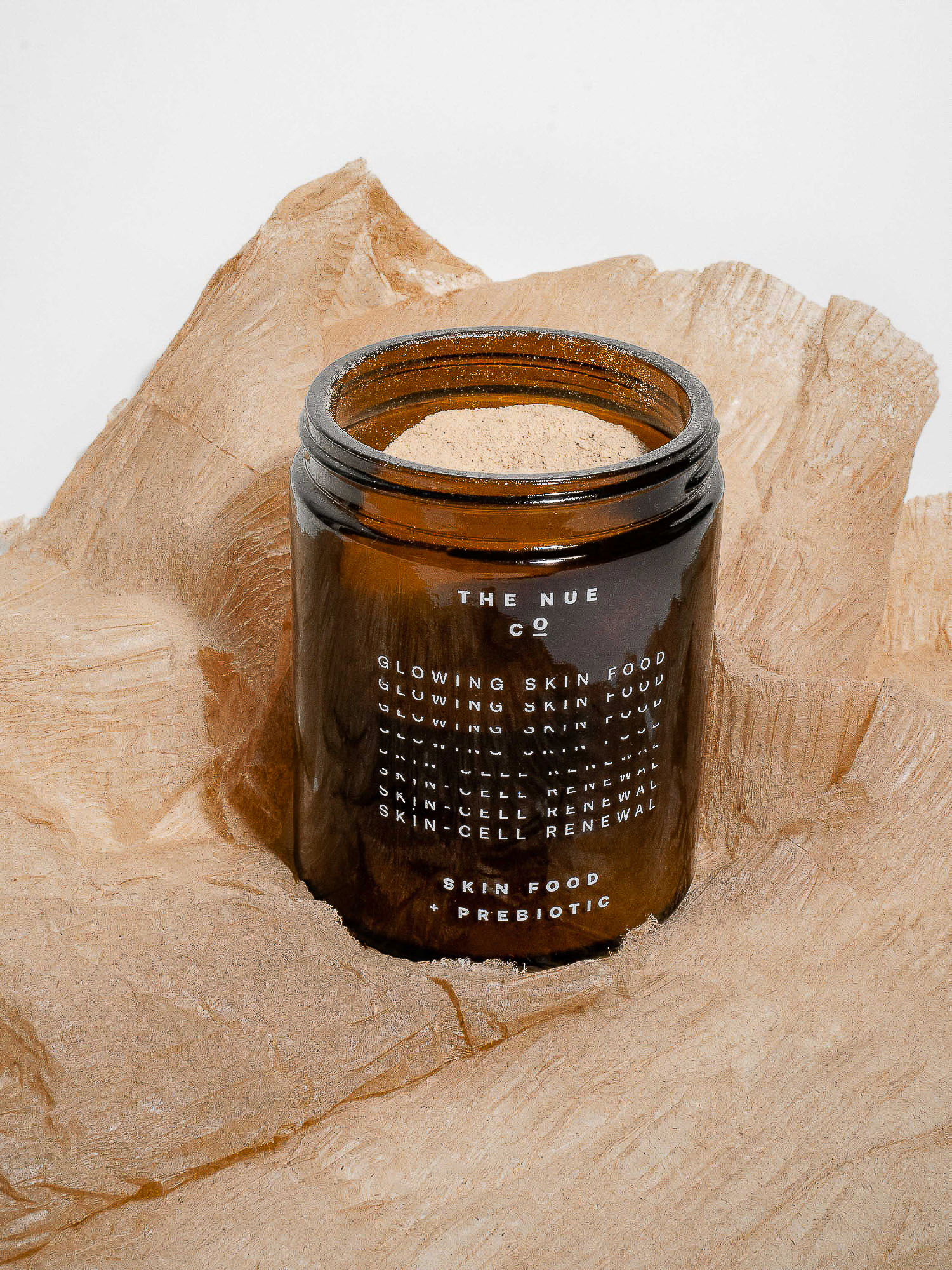 Brown jar of glowing skin food on a beige paper background, clean minimalist shot, product photography for the beauty and skincare industry.