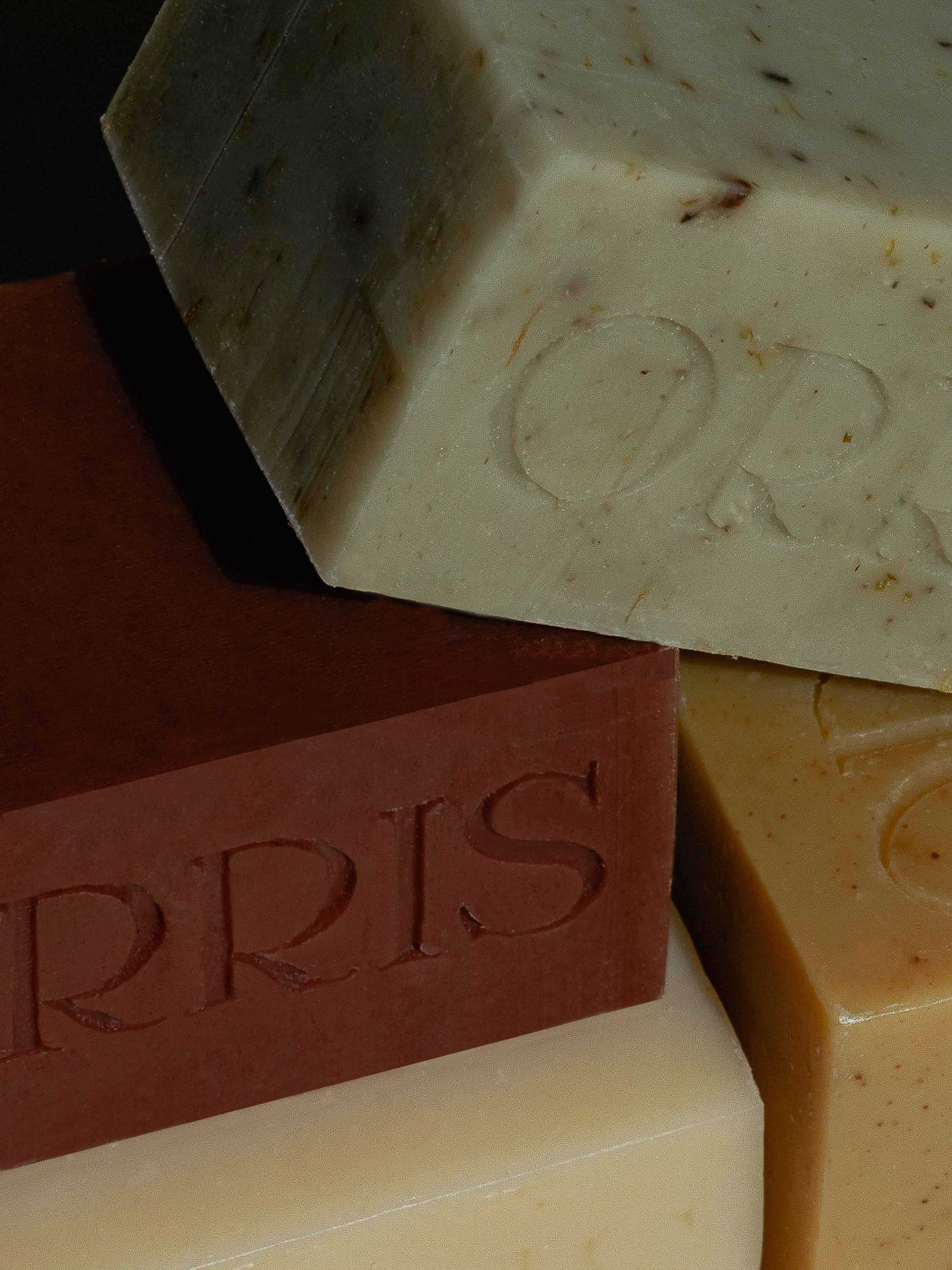 Stacked bars of handmade soaps with embossed lettering in earth tones, creating a textured, artisanal surface.