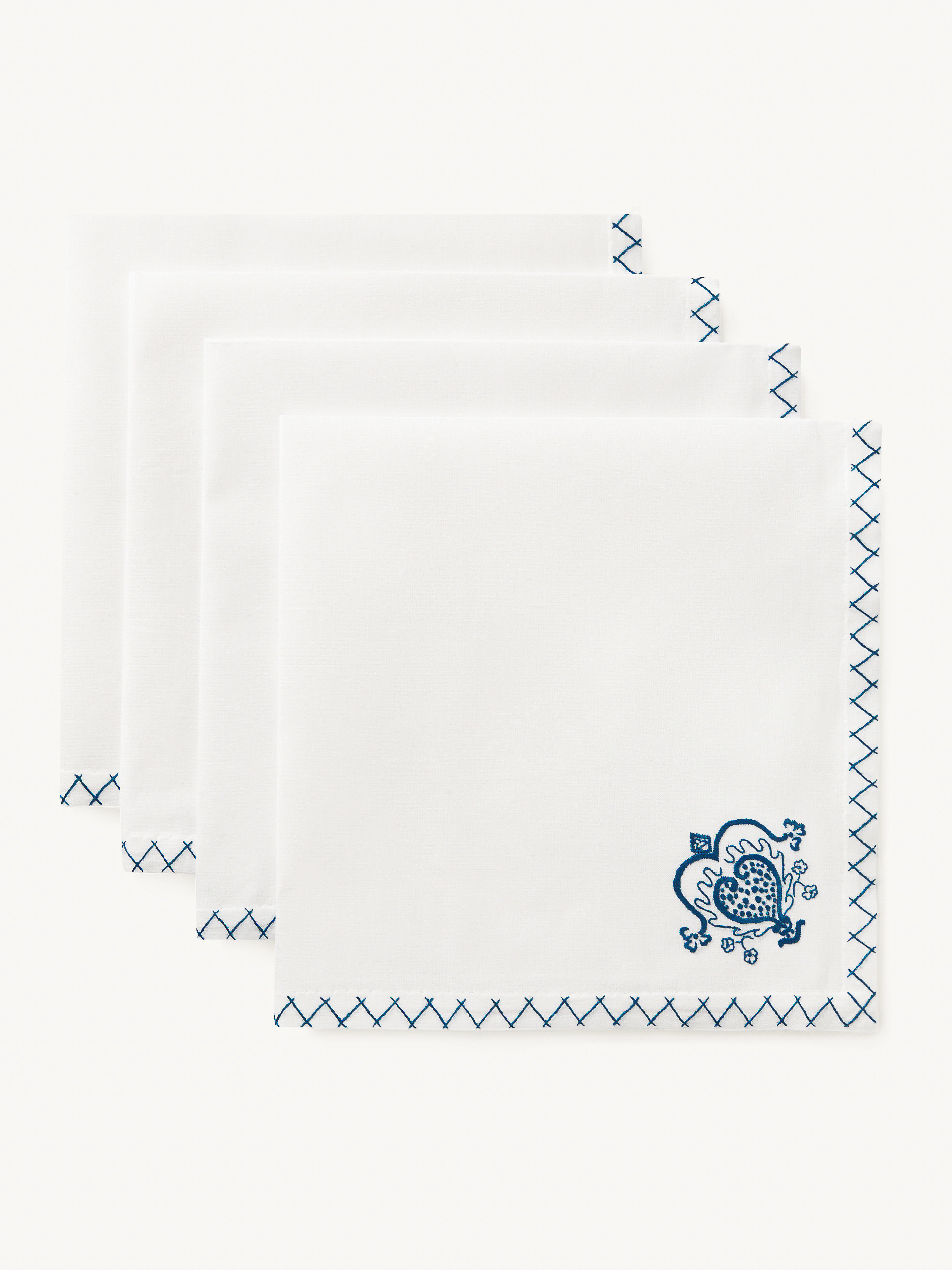 Stack of white linen napkins with blue decorative stitching and an ornate floral design in the corner, flat lay product shot.