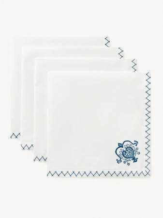 Stack of white linen napkins with blue decorative stitching and an ornate floral design in the corner, flat lay product shot.