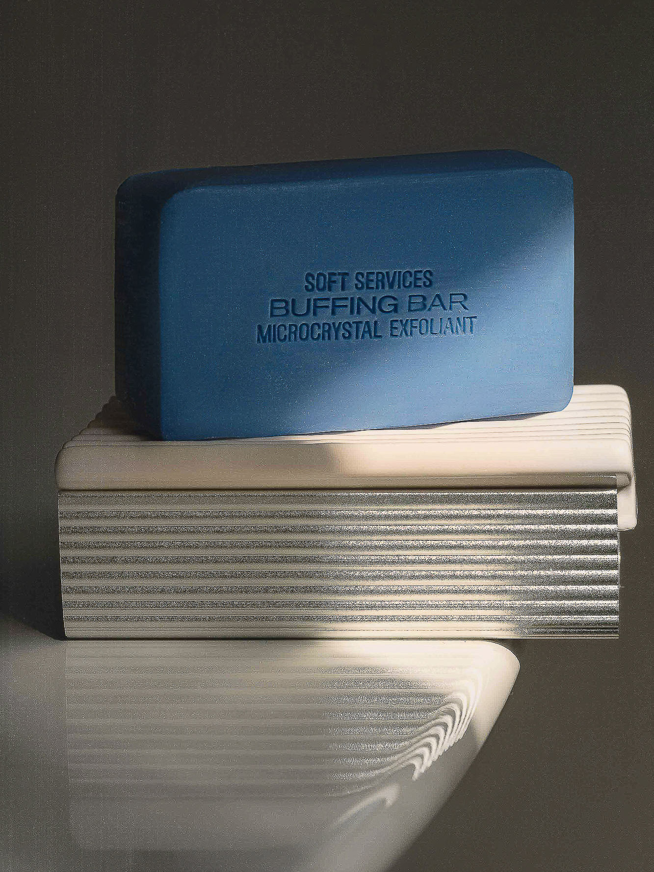 Close-up still life of a blue soap bar on top of a ridged white container in studio lighting, showcasing minimalist beauty product photography.