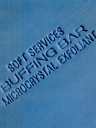 Close-up detail of debossed lettering on a textured blue Soft Services Buffing Bar microcrystal exfoliant soap.