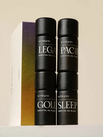 Four VITRUVI essential oil blend bottles with black caps and white labels, stacked in pairs, alongside a partial product box.