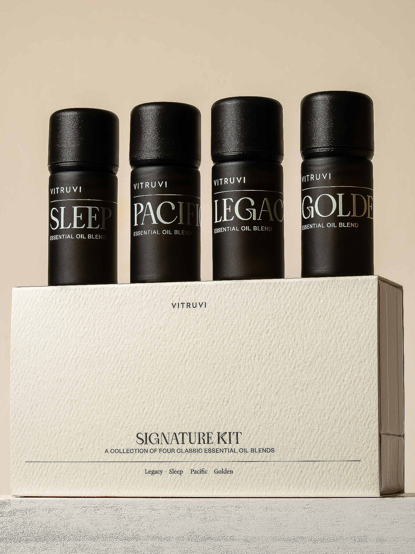 Four Vitruvi essential oil bottles on a Signature Kit box. The oils are labeled Sleep, Pacific, Legacy, and Golden.