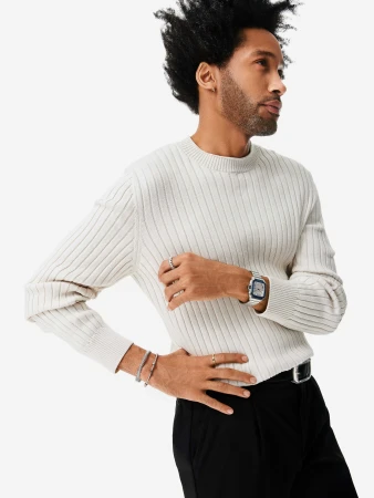 Black man wearing a cream ribbed knit sweater and silver luxury watch against a white seamless studio backdrop.