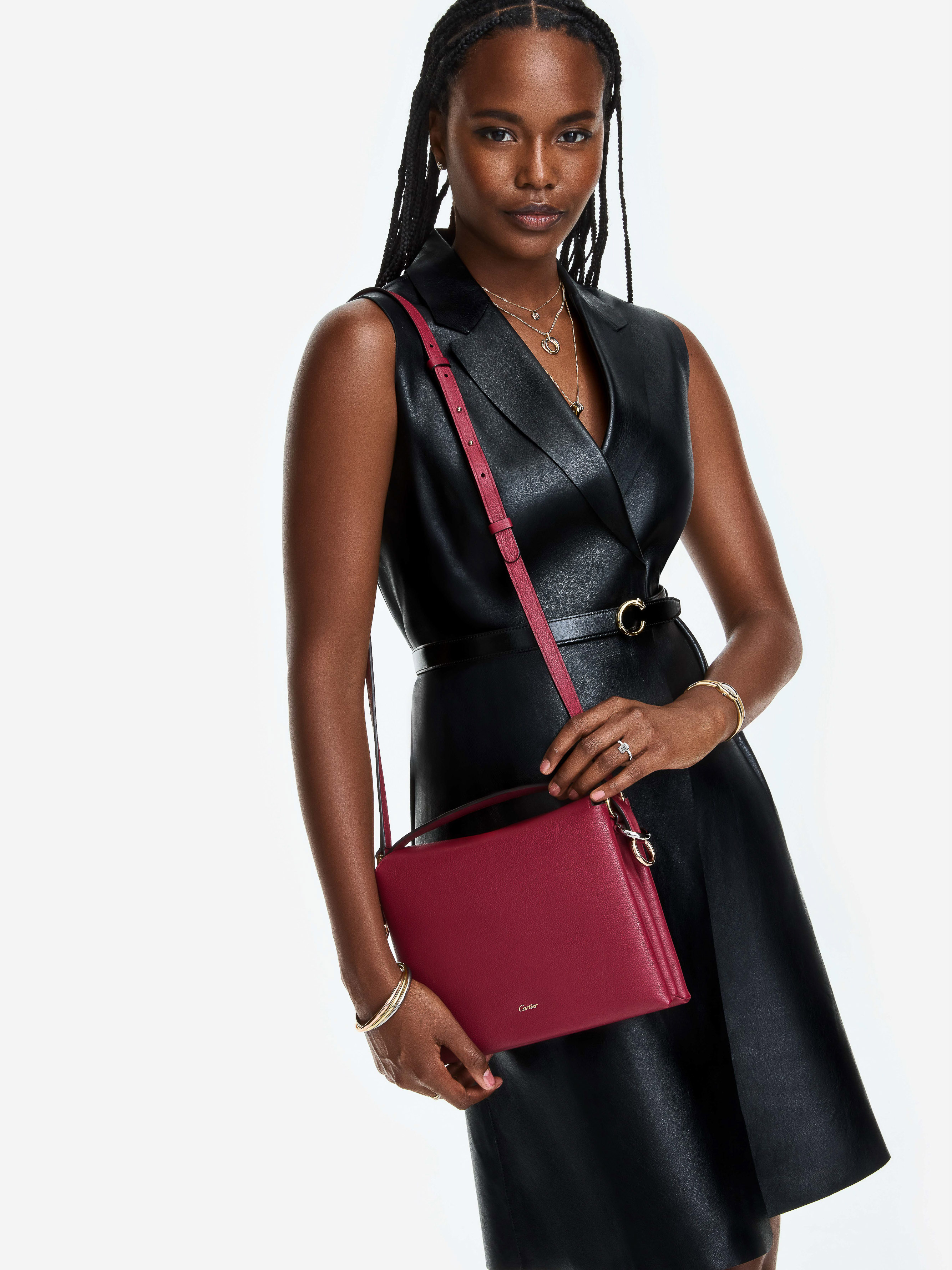 A stylish Black woman in a black dress wearing a burgundy purse stands against a white backdrop, showcasing fashion and elegance.