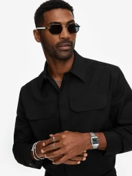 Black man wearing sunglasses, black shirt, silver watch, and rings against a white seamless background for Cartier