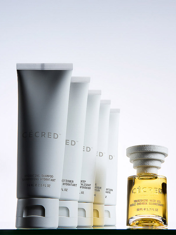 Ceced brand beauty product array. White tubes of shampoo, conditioner, & hair treatment, with a bottle of hair oil on glass.