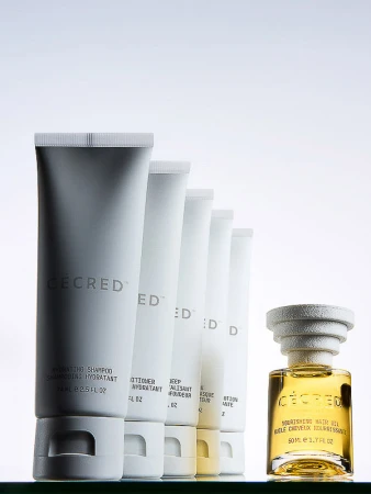 Ceced brand beauty product array. White tubes of shampoo, conditioner, & hair treatment, with a bottle of hair oil on glass.