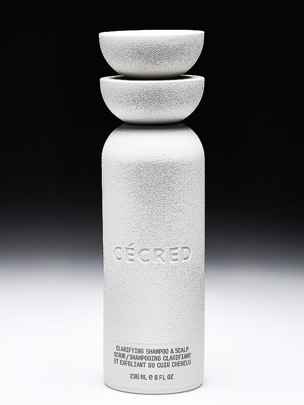 White bottle of clarifying shampoo and scalp scrub, topped with two small bowls, set against a gradient black to white background.