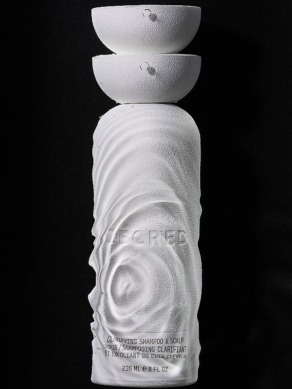 White shampoo bottle with sculptural design and two white half-sphere lids stacked on top against a dark black background. Product shot.