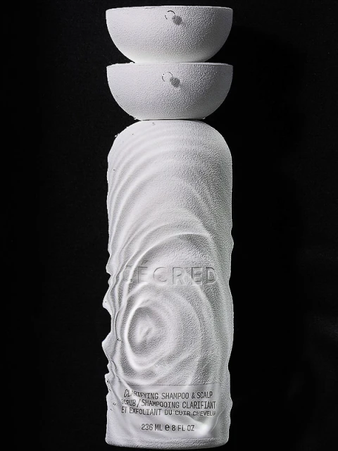 White shampoo bottle with sculptural design and two white half-sphere lids stacked on top against a dark black background. Product shot.