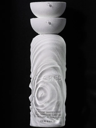 White shampoo bottle with sculptural design and two white half-sphere lids stacked on top against a dark black background. Product shot.