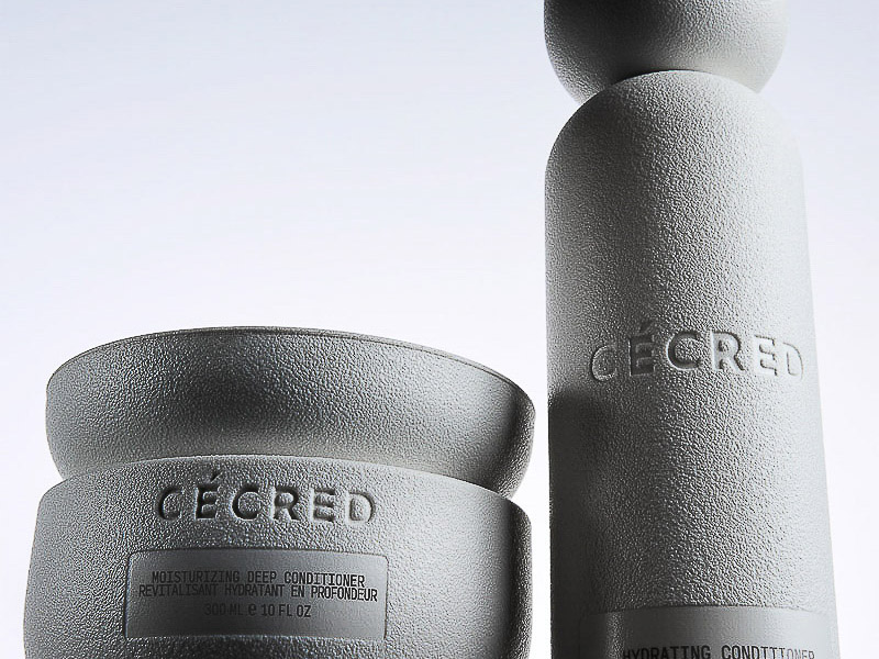 Close-up product shot of two textured, light gray Ceced brand hair-care containers, a round cream and a tall bottle, on a white background.
