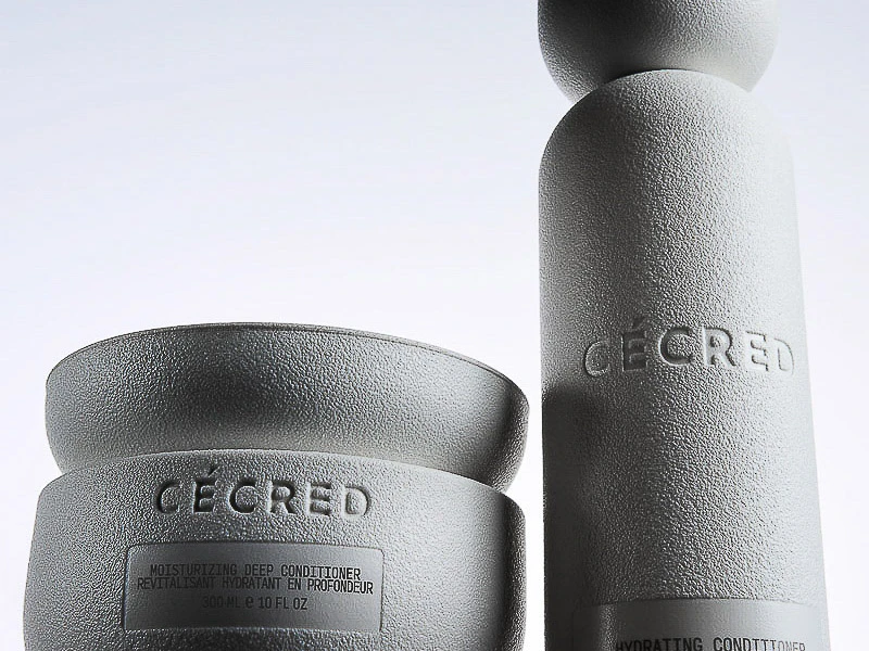 Close-up product shot of two textured, light gray Ceced brand hair-care containers, a round cream and a tall bottle, on a white background.