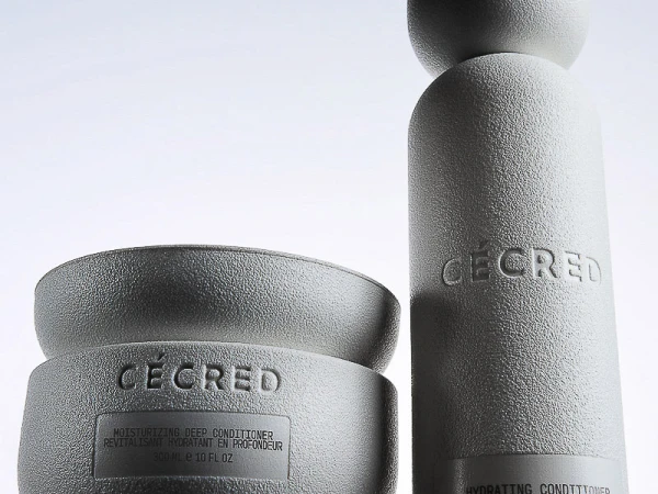 Close-up product shot of two textured, light gray Ceced brand hair-care containers, a round cream and a tall bottle, on a white background.