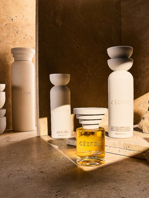 Still life of CÉCRED haircare bottles in neutral tones on a stone surface, with warm lighting highlighting the product design.