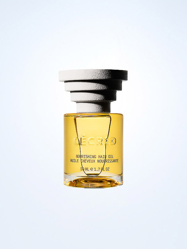 Close-up of a 'Décred' nourishing hair oil bottle with a layered white cap, showcasing its golden liquid and label against a light backdrop.