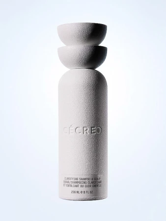 White textured CÉCRED clarifying shampoo bottle with stacked spherical lid, against a gradient background. Beauty product shot.