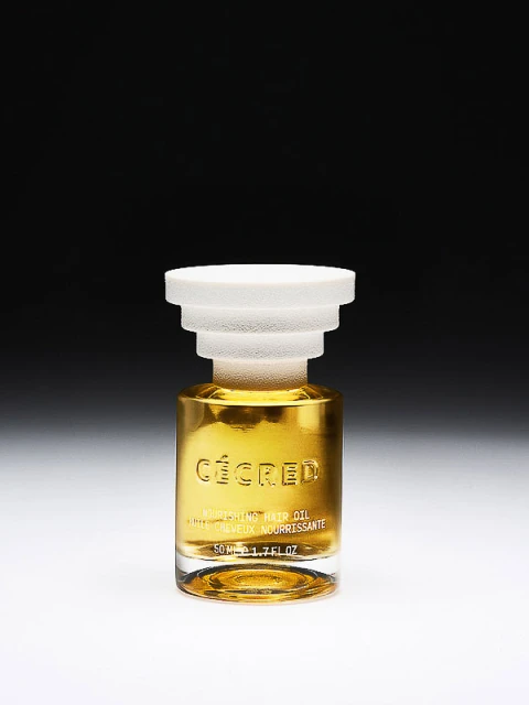 A bottle of hair oil by Cécéd against a dark gradient background, featuring a glass body, a white cap, and golden-colored oil inside.