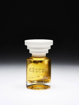 A bottle of hair oil by Cécéd against a dark gradient background, featuring a glass body, a white cap, and golden-colored oil inside.