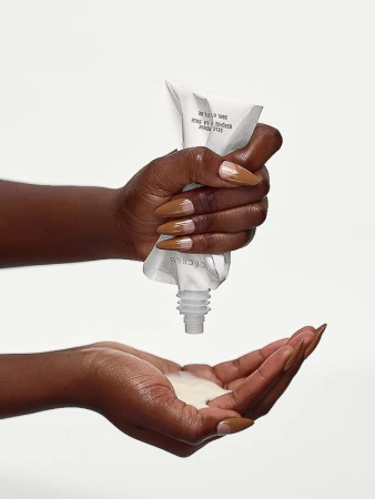 Close-up of dark-skinned hands squeezing a white tube and dispensing white lotion, showcasing skincare and beauty products in a studio setting.