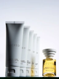 Row of Cécred haircare tubes and a small bottle of golden hair oil arranged on a reflective surface against a white background.