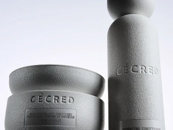 Close-up of textured stone-finish Cécred conditioner jar and bottle with debossed lettering against a light background.