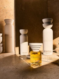 Cécred haircare bottles and golden hair oil arranged on textured travertine stone slabs with dramatic angled shadows.