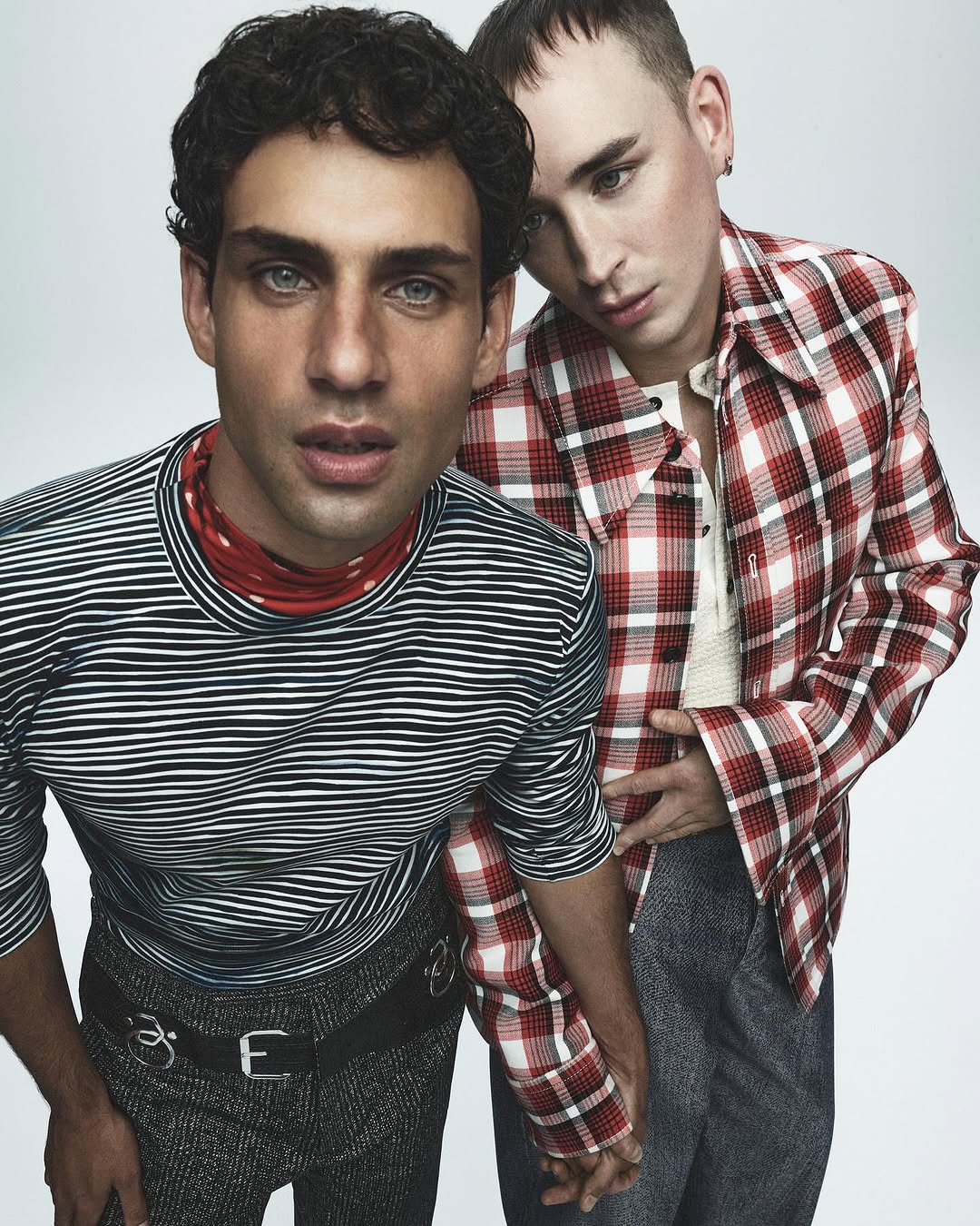 Two men posing together for Russh editorial, one wearing a striped top and the other in a red plaid shirt.