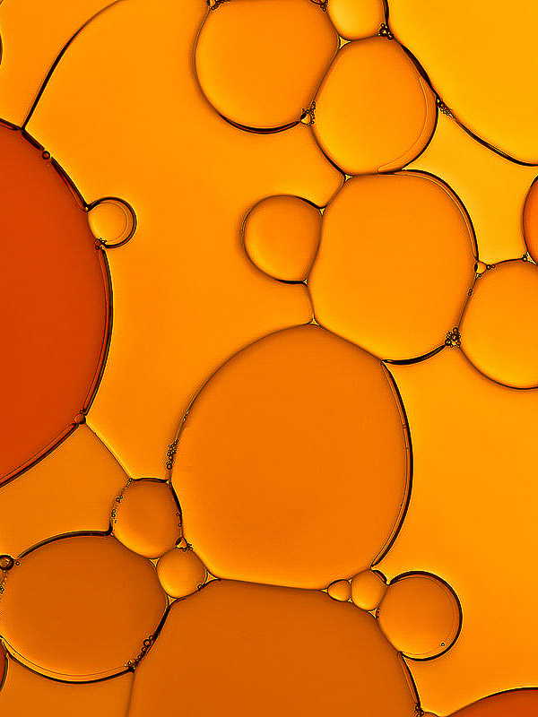 Macro photograph of vibrant orange oil and liquid bubbles of varying sizes creating an abstract cellular-like background.