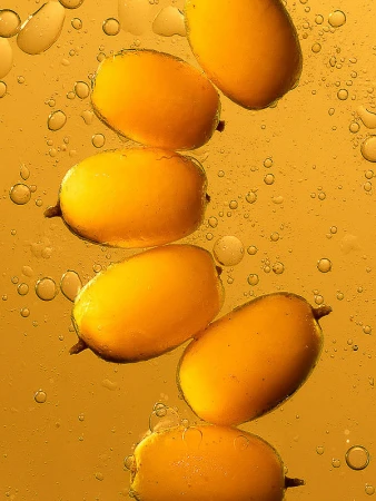 Stack of kumquats in transparent liquid with bubbles. Food photography shows the fruit suspended in golden liquid with light and shadows.