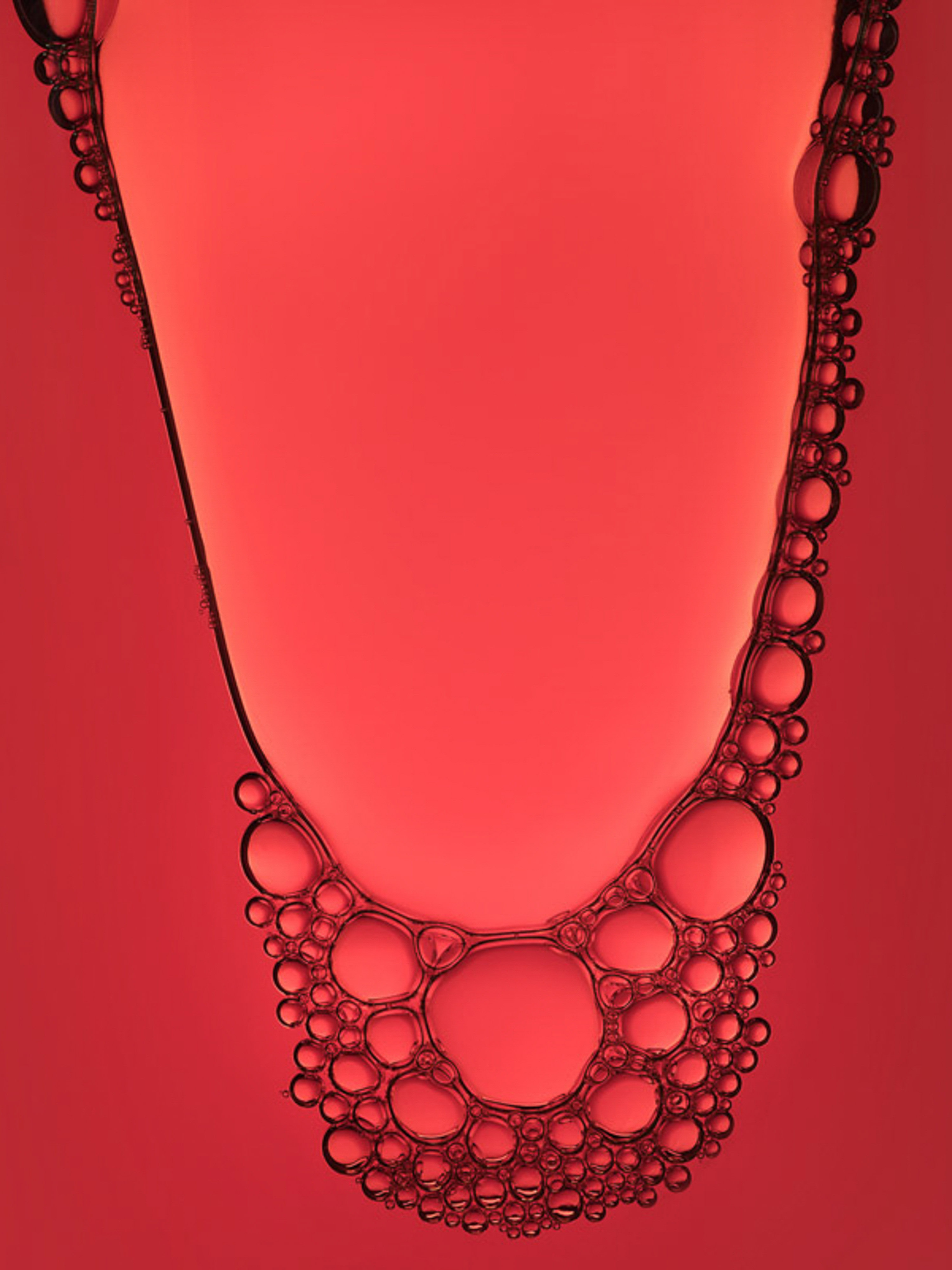 Abstract close-up shot of liquid with small and large red-tinted bubbles forming an organic pattern against a red background.