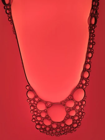Abstract close-up shot of liquid with small and large red-tinted bubbles forming an organic pattern against a red background.