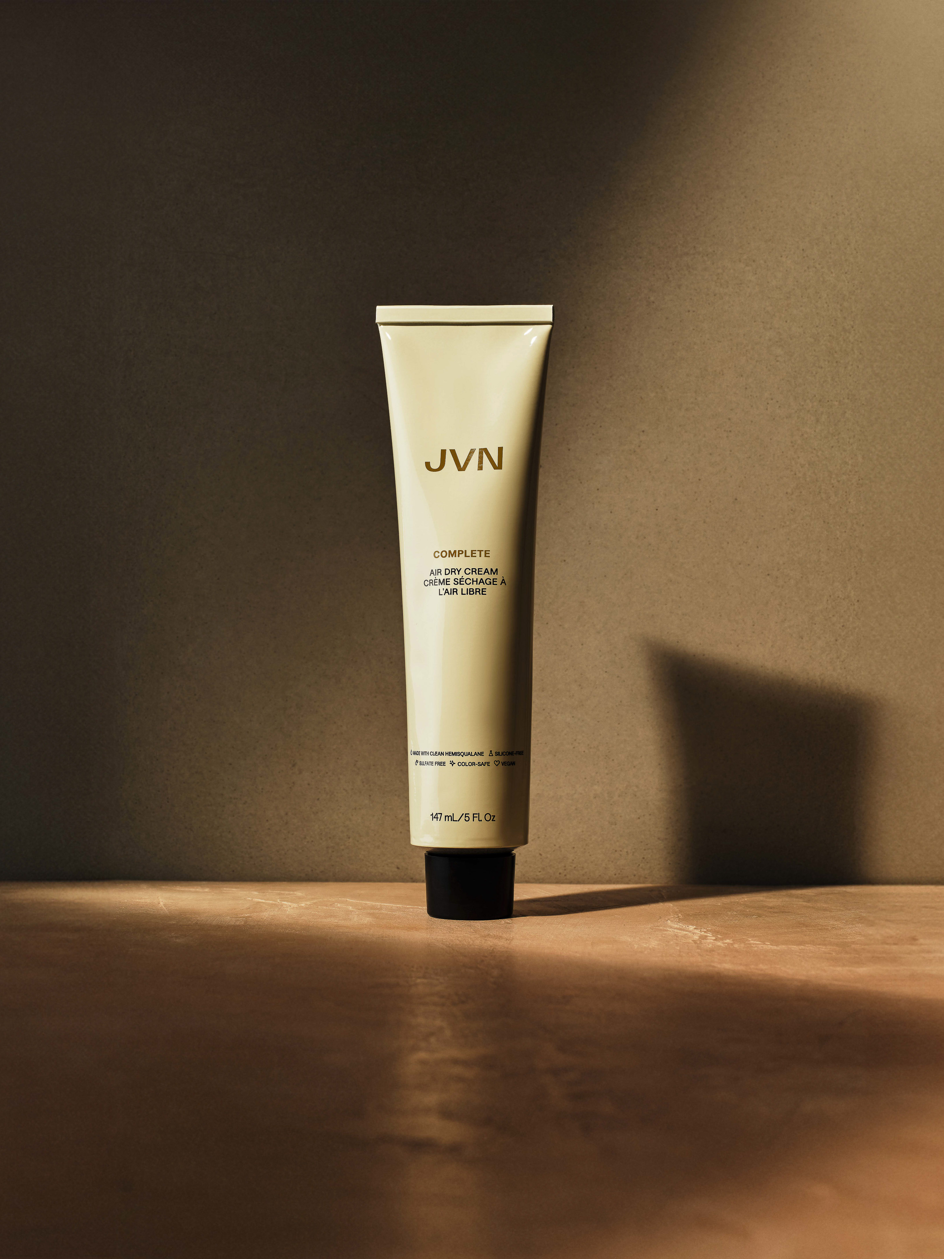 JVN Complete Air Dry Cream in an off-white tube with black cap on a surface, lit by soft light against a neutral background.