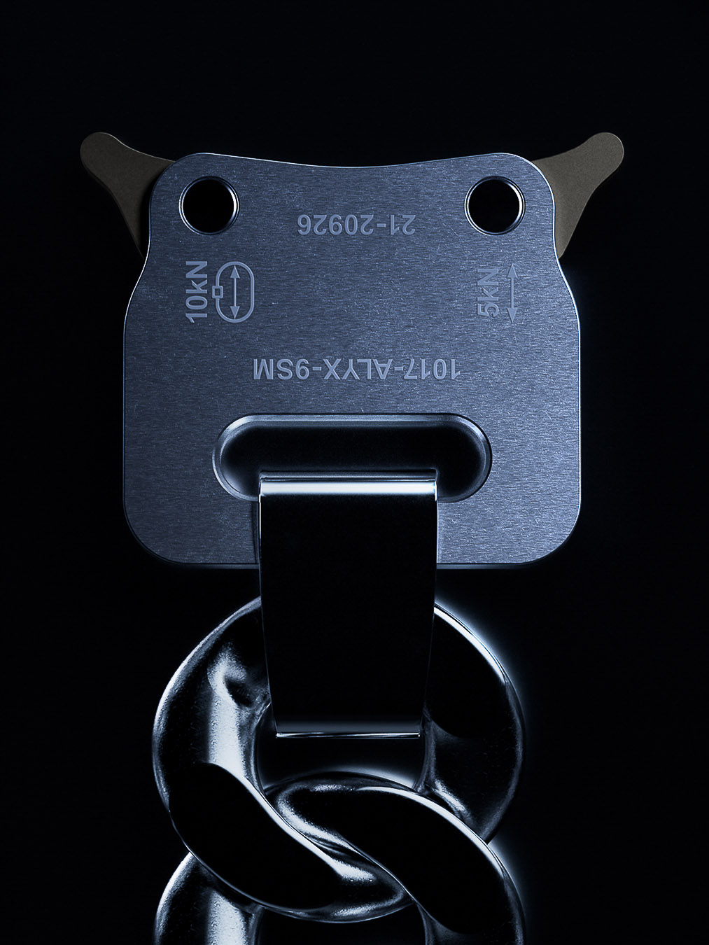 Silver metal ALYX buckle and chain on a dark background, close-up shot showcasing the industrial design and material.