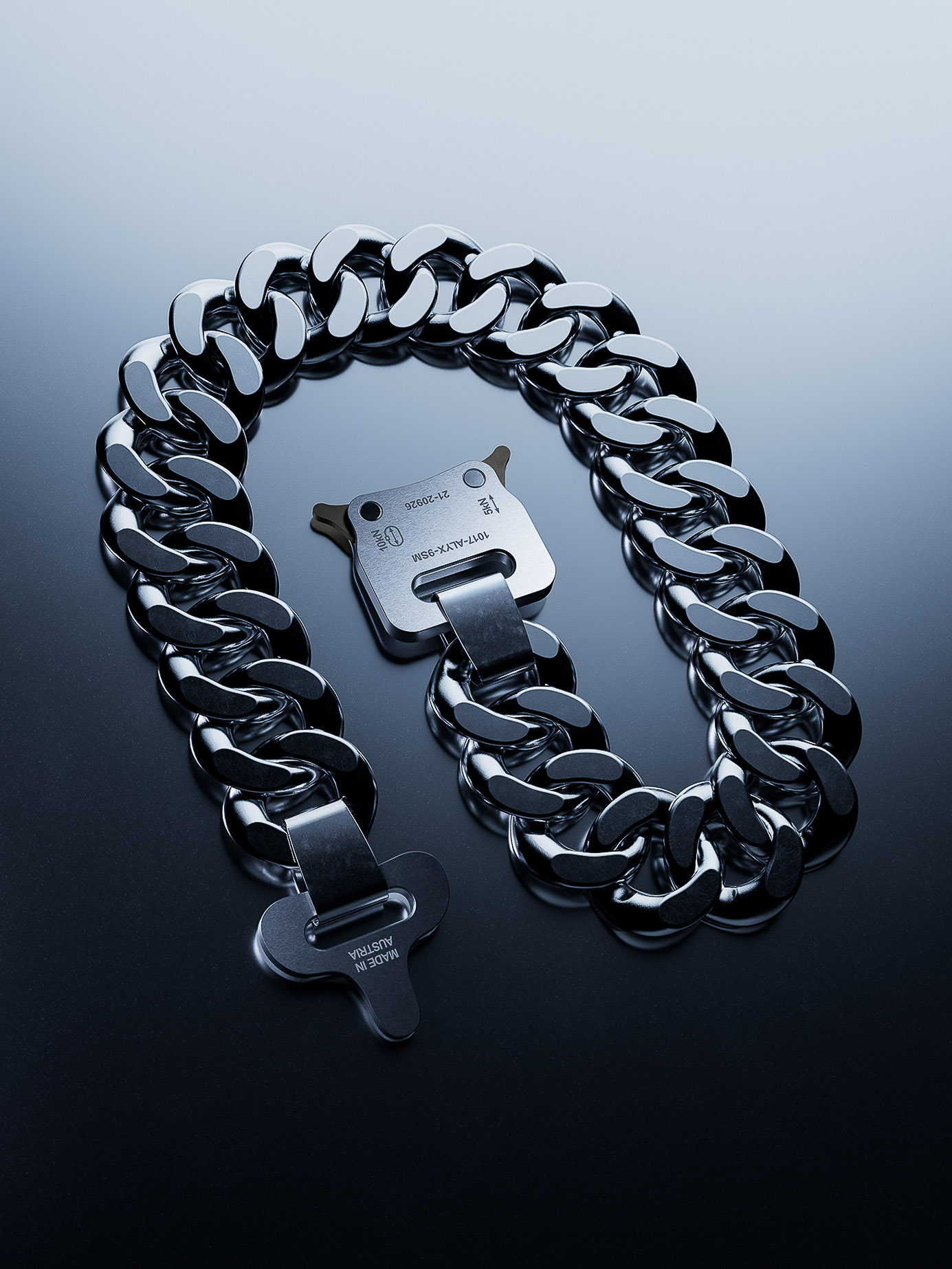 A metal chain link necklace with buckle clasp is lying on a glossy surface in an eye-level studio shot with dark and light gradients.