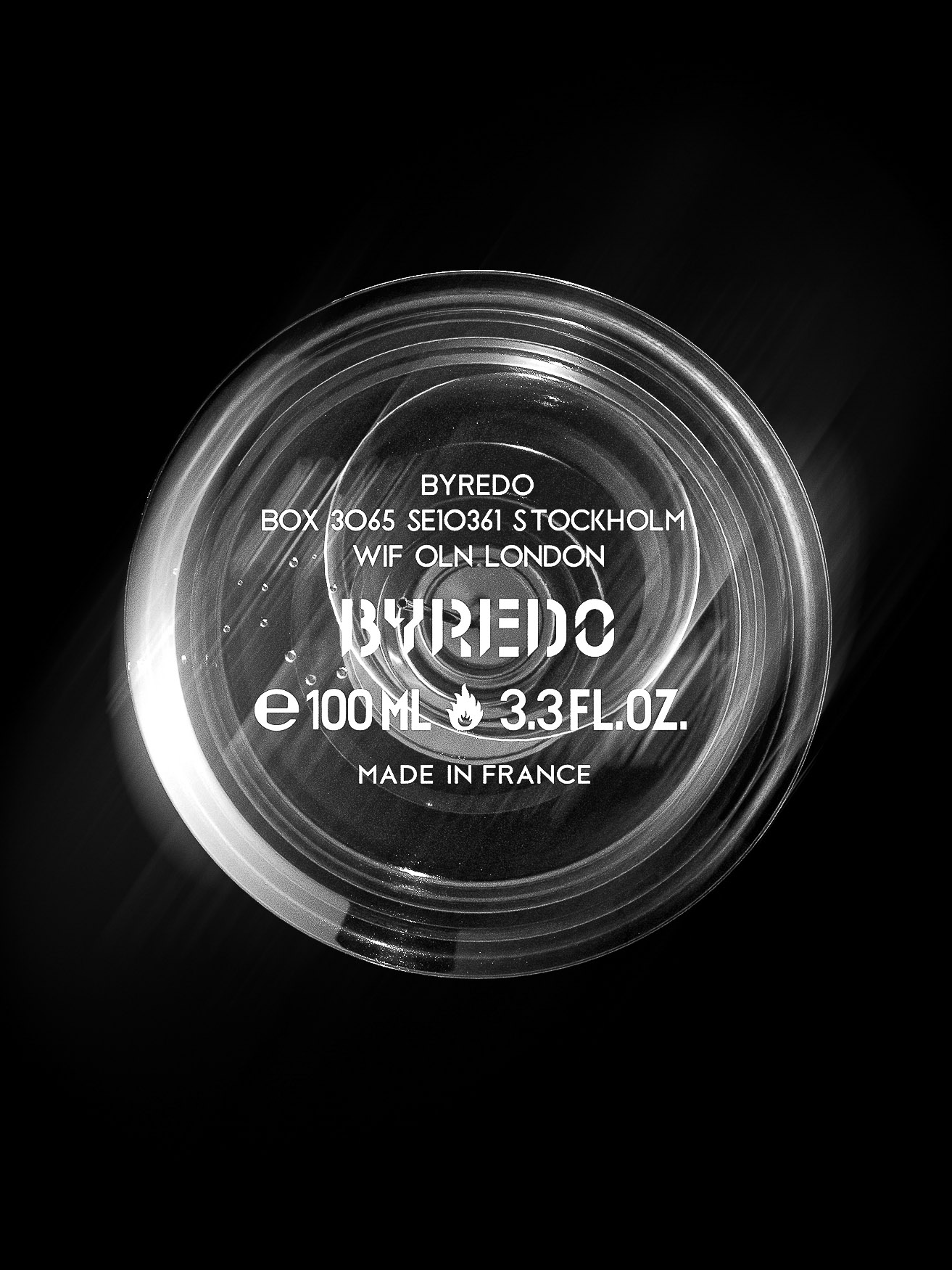 Close-up of a Byredo perfume bottle against a black background. The clear glass shows the brand name, volume, and country of origin.
