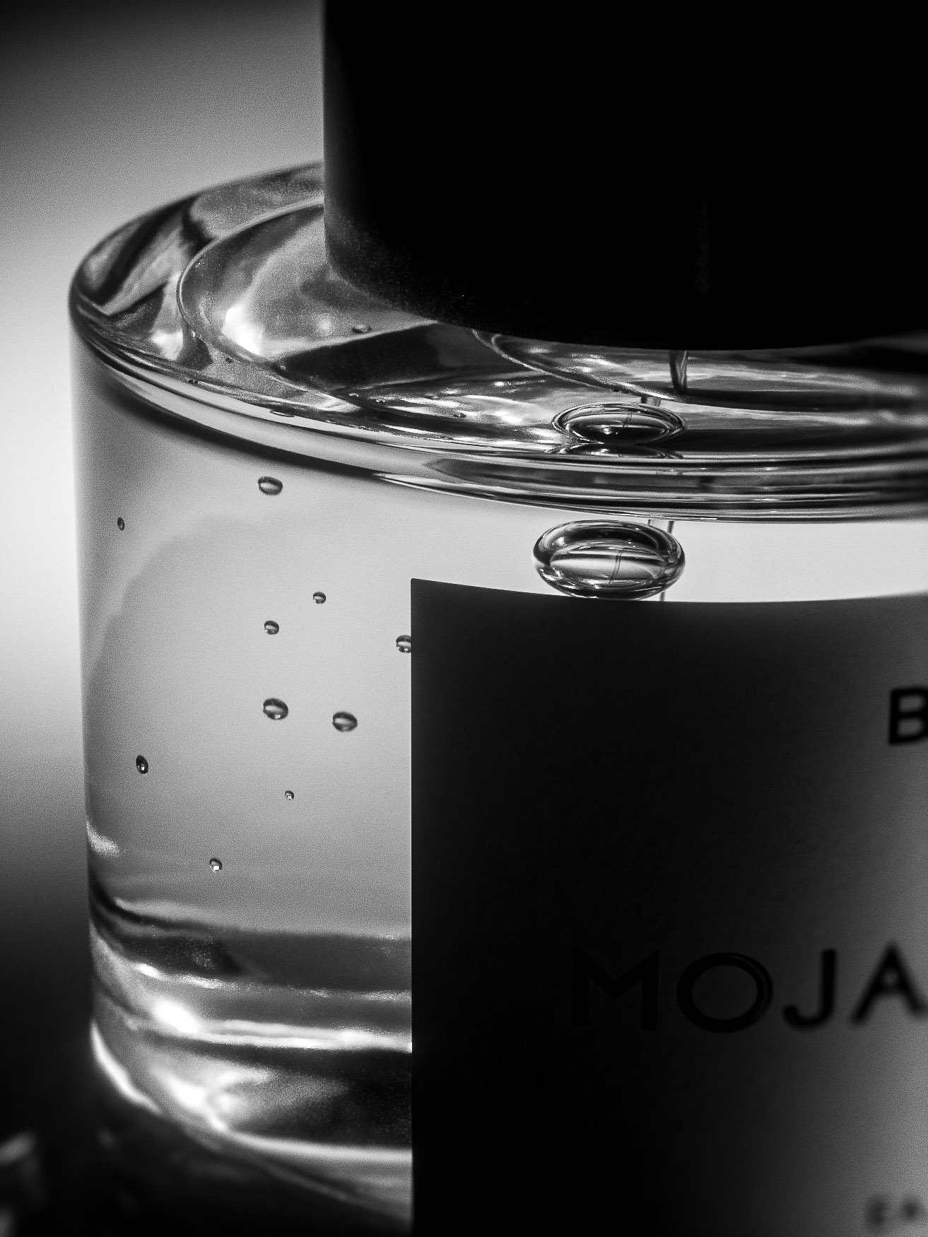 Close-up shot of a transparent bottle of mojave ghost fragrance with a black cap and label, showcasing minimalist beauty in monochrome.