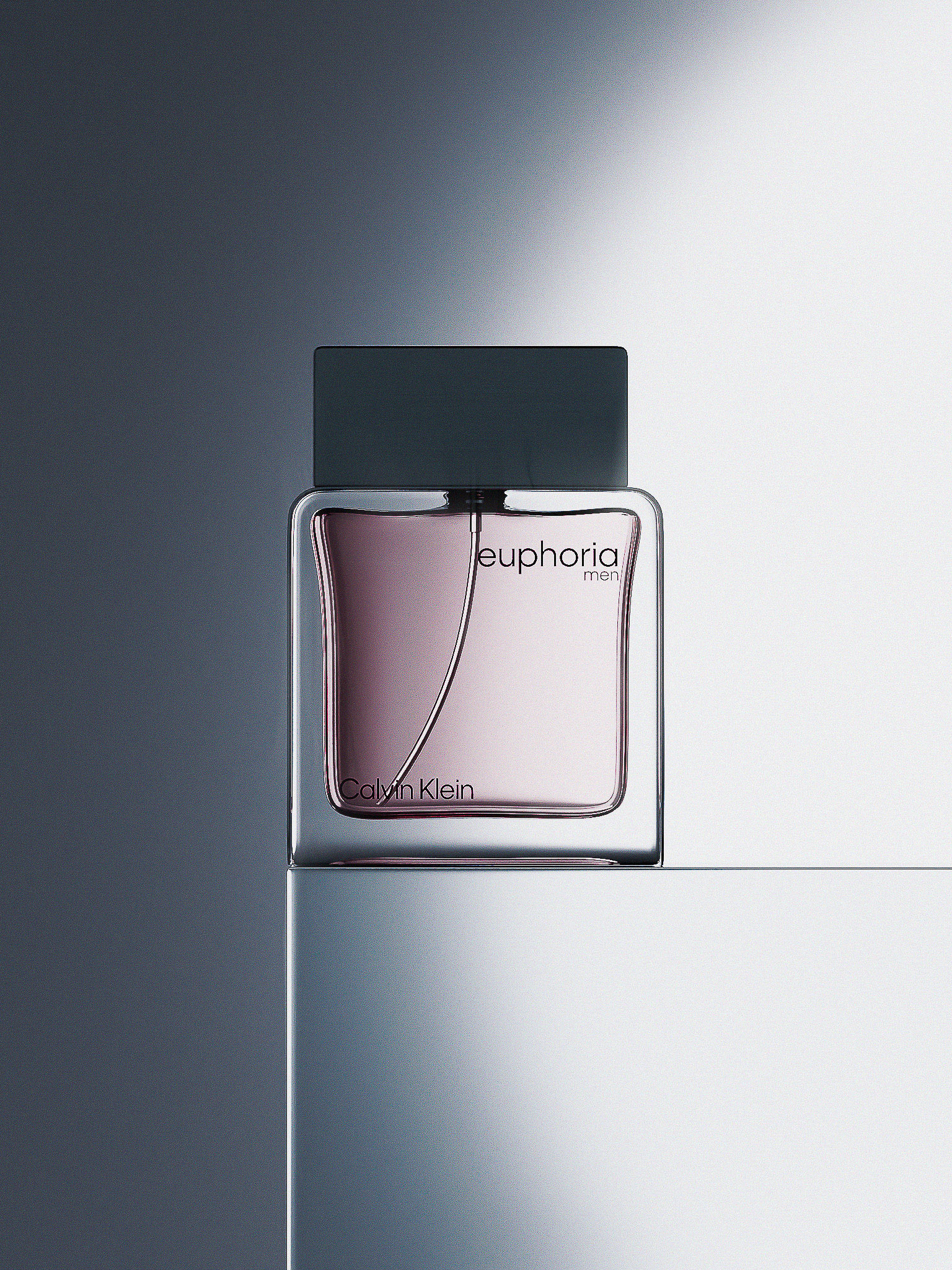 Close-up studio shot of a Calvin Klein Euphoria men's fragrance bottle featuring a glass container and gray cap on a gray surface.