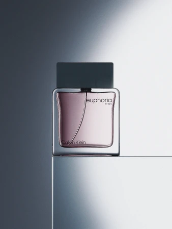Close-up studio shot of a Calvin Klein Euphoria men's fragrance bottle featuring a glass container and gray cap on a gray surface.