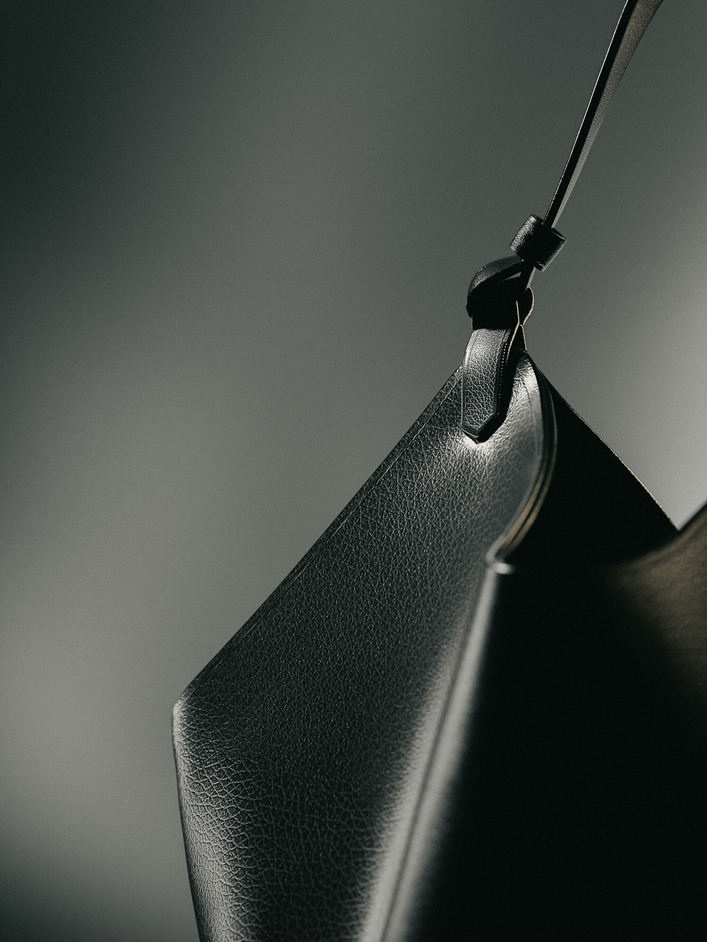 Close-up product shot of a black leather purse with a strap against a dark grey background, product photography, studio lighting.