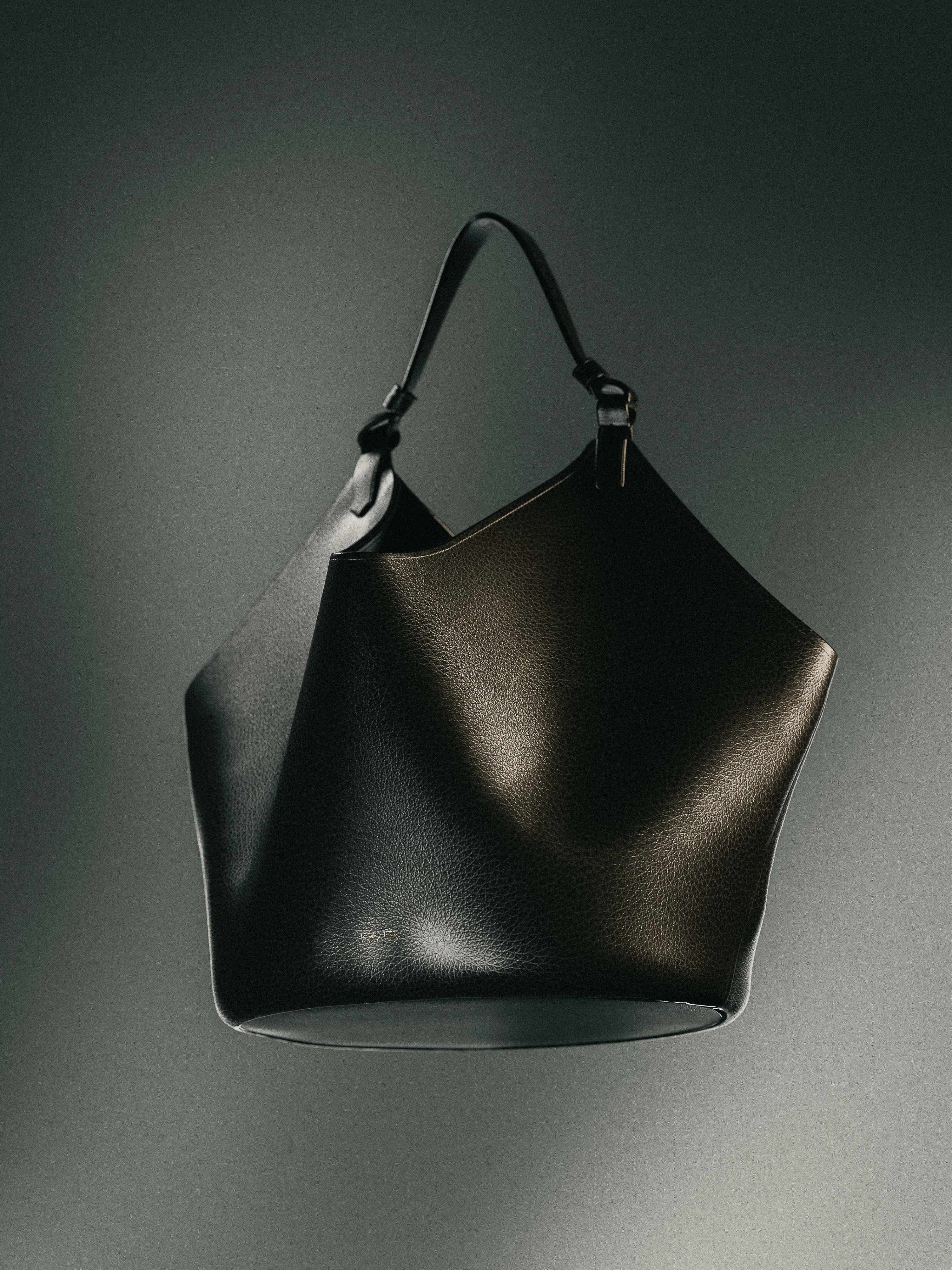 Studio shot of a black leather tote bag with a single strap against a dark gradient backdrop with subtle lighting.