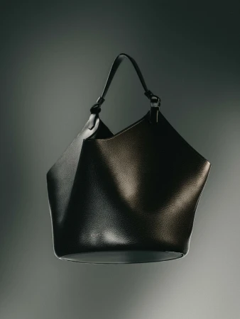 Studio shot of a black leather tote bag with a single strap against a dark gradient backdrop with subtle lighting.