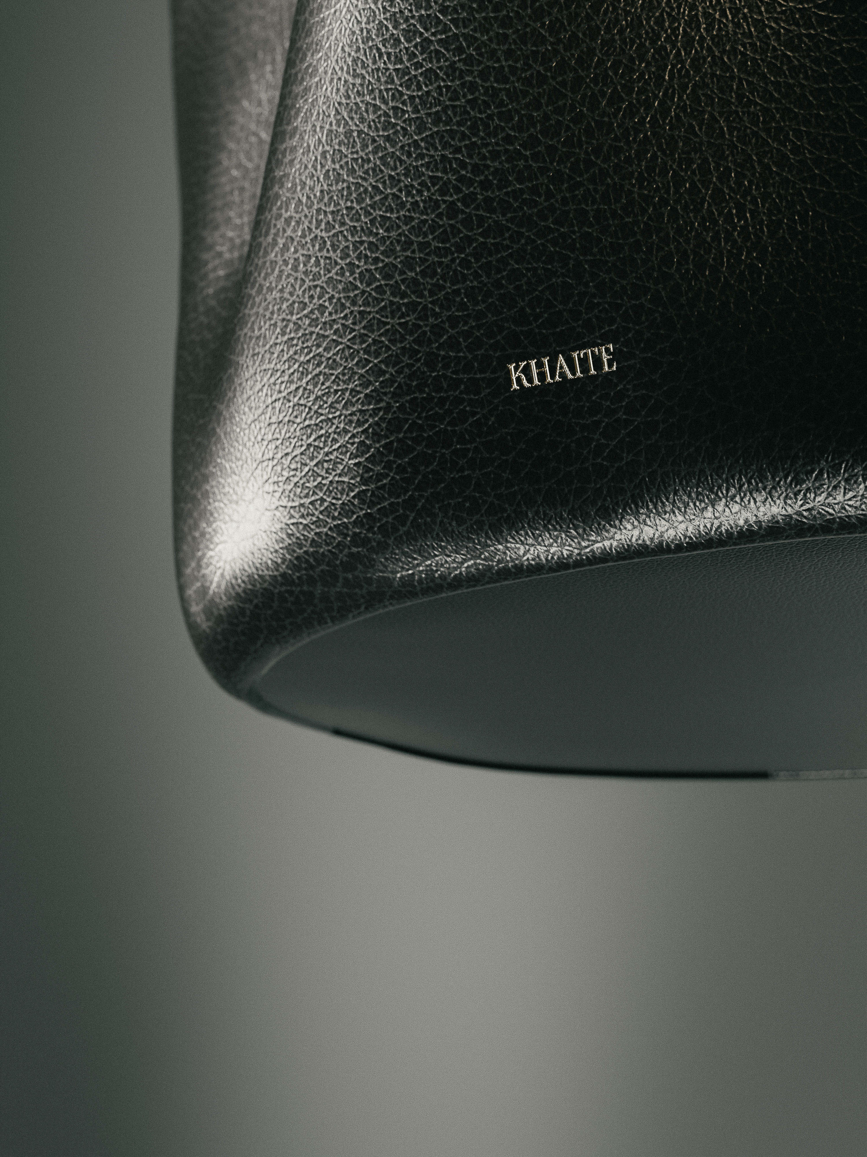 Close-up studio shot of a Khaite black leather hobo bag, showing off the material's texture and the brand's logo in a minimalist setting.