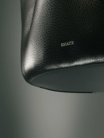 Close-up studio shot of a Khaite black leather hobo bag, showing off the material's texture and the brand's logo in a minimalist setting.