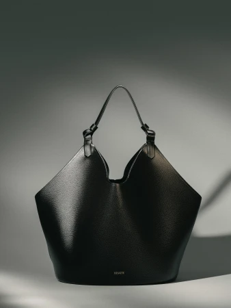Black leather tote bag with top handles on a neutral background in a studio setting, product shot for fashion accessory, Khaite branding visible.