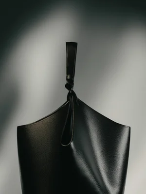 Close-up of a structured black pebbled leather tote bag with a looped handle against a diffused grey gradient background.