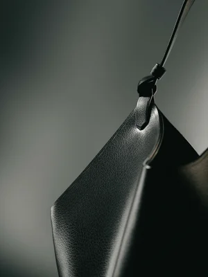 Close-up of a black leather handbag with a thin strap and knotted detail against a smooth grey gradient background.